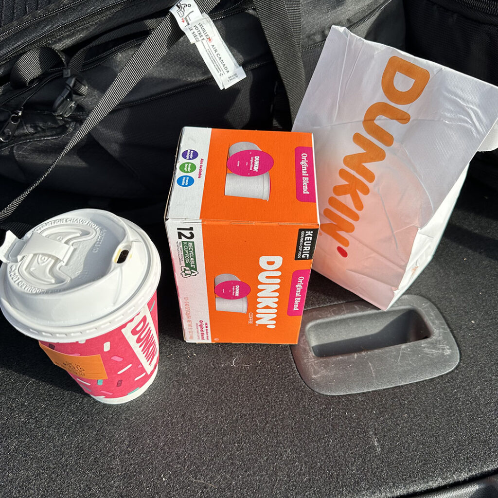 Dunkin' Donuts coffee and a box of donuts with a to-go bag on a car seat, showcasing a quick coffee and snack break for on-the-go consumers that are shopping in erie pa